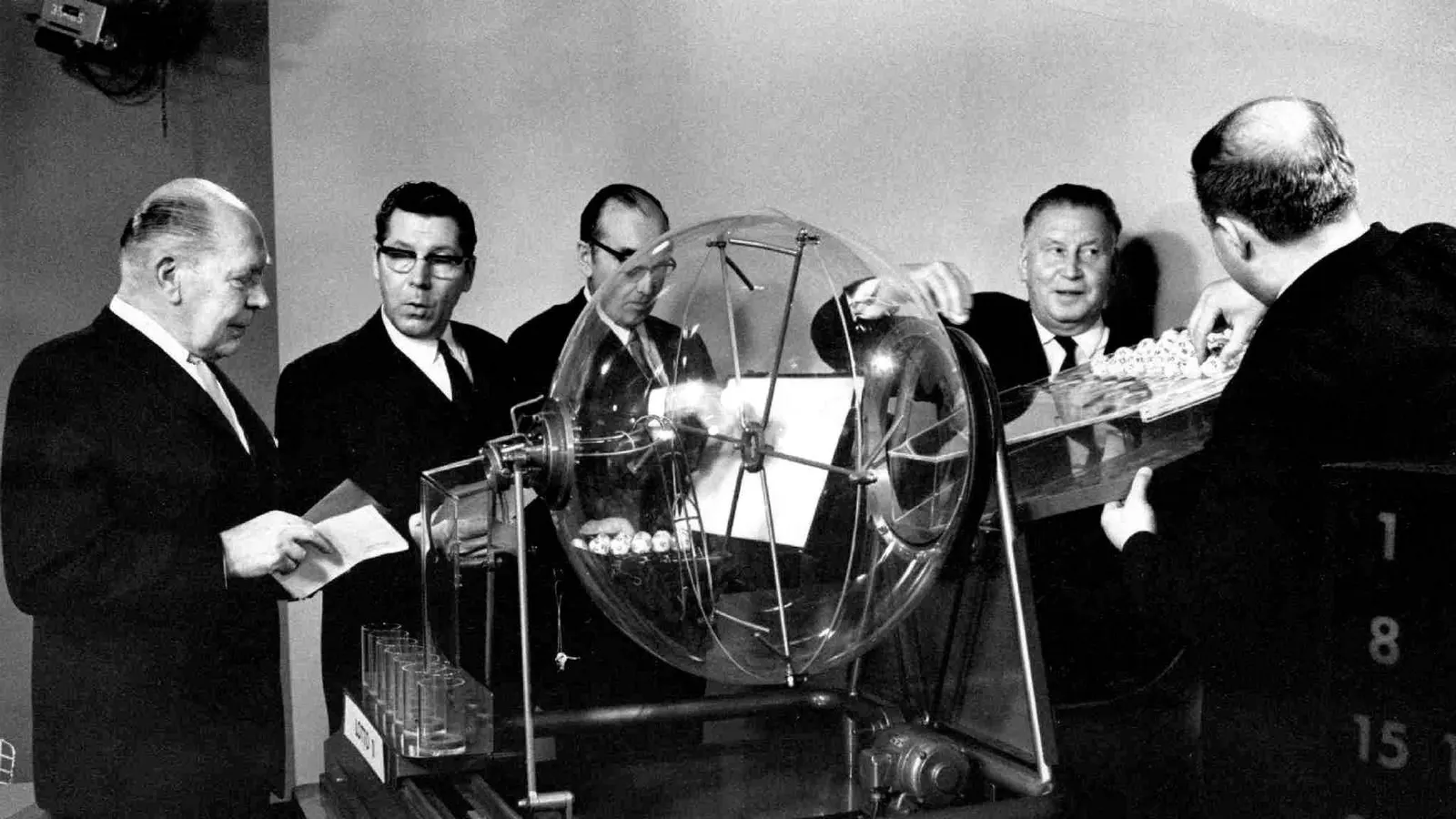 Tirage d'une loterie en Finlande en 1971 : cinq hommes autour d'un globe transparent contenant des boules numérotées